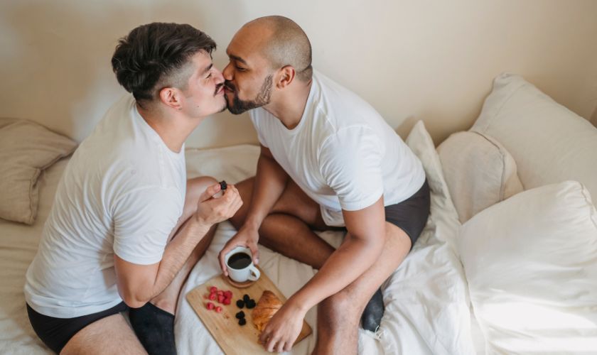 Cómo reconstruir una vida sexual saludable tras la adicción al sexo: dos hombres sonrientes se da un beso antes de desayunar en la cama.